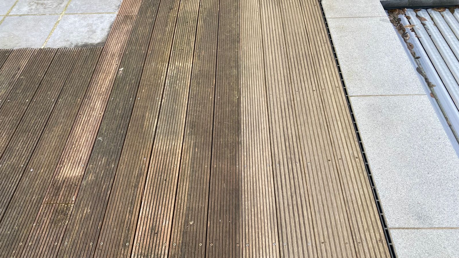 Droog opschuren van houten terras, rechts geschuurd, links groen en vuil.