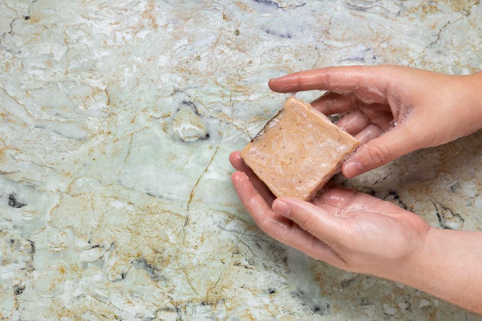 Handen wassen met zeep boven een geaderd oppervlak: bij de keuze voor natuursteen, composiet of keramiek in de badkamer telt het contact met water en zeep.