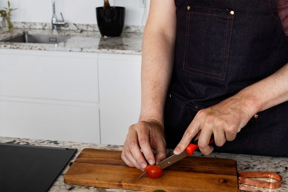 Tomaten snijden op een houten snijplank: bij de keuze voor een keukenblad in natuursteen, composiet of keramiek telt hoe je dagelijks kookt.